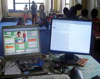 Mein Schreibtisch mit Laptop und Zusatz-Bildschirm; im Hintergrund spielen Kinder.